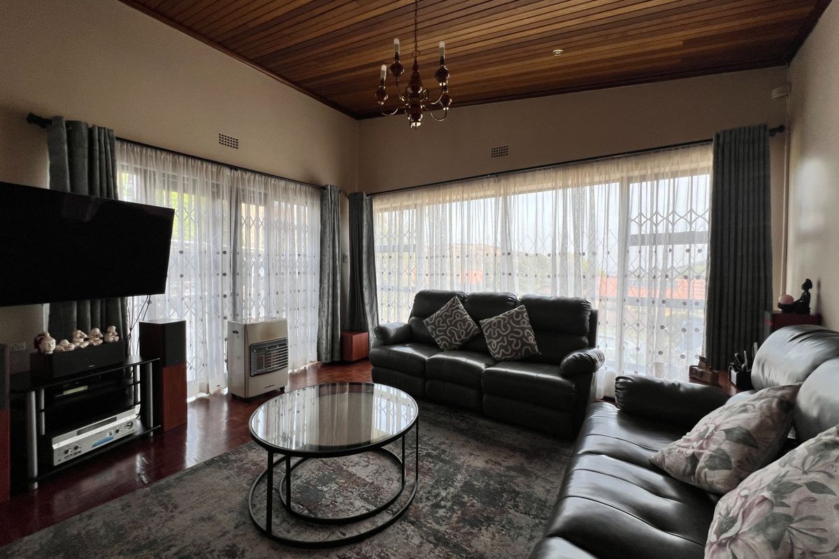 Spacious living room featuring a warm timber ceiling, hardwood flooring, and large windows with security gates, offering a comfortable and well-maintained living space.