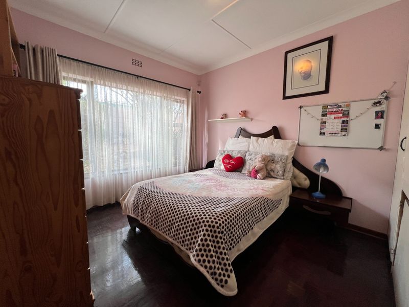 A bedroom featuring dark parquet flooring, a built-in headboard, and large windows with curtain rails.