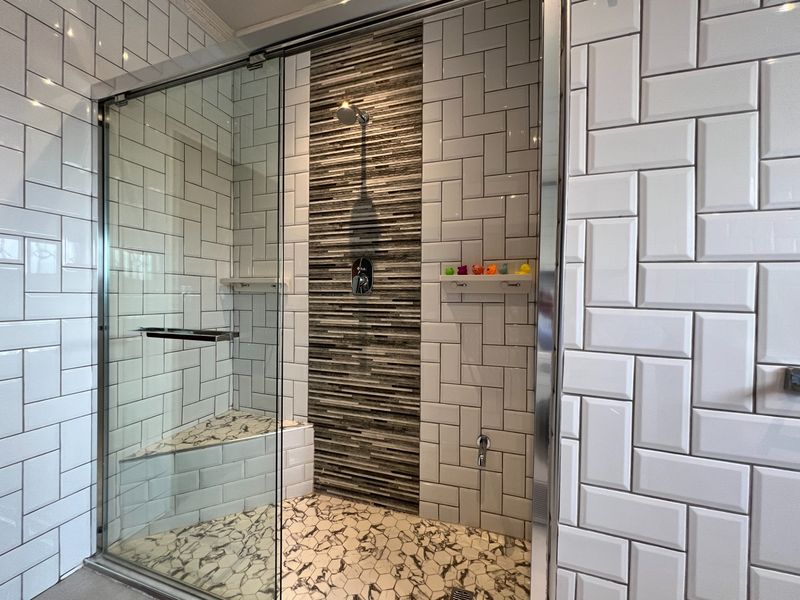 Modern walk-in shower featuring white subway wall tiles, a decorative mosaic feature wall, hexagonal floor tiles, and a glass enclosure.