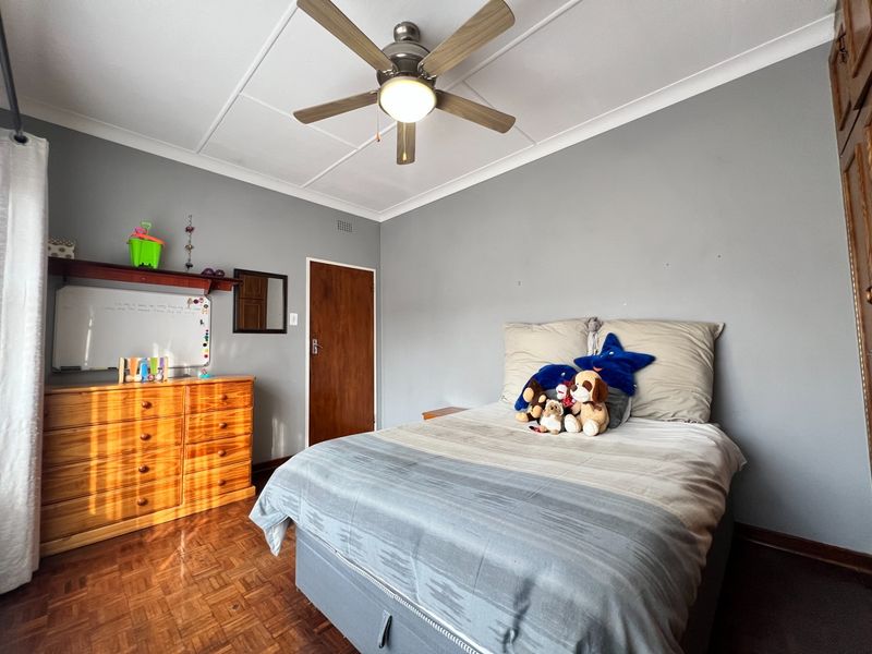 A bedroom featuring parquet flooring, a ceiling fan, and built-in cupboard storage, finished with neutral grey walls and coved ceiling detailing.