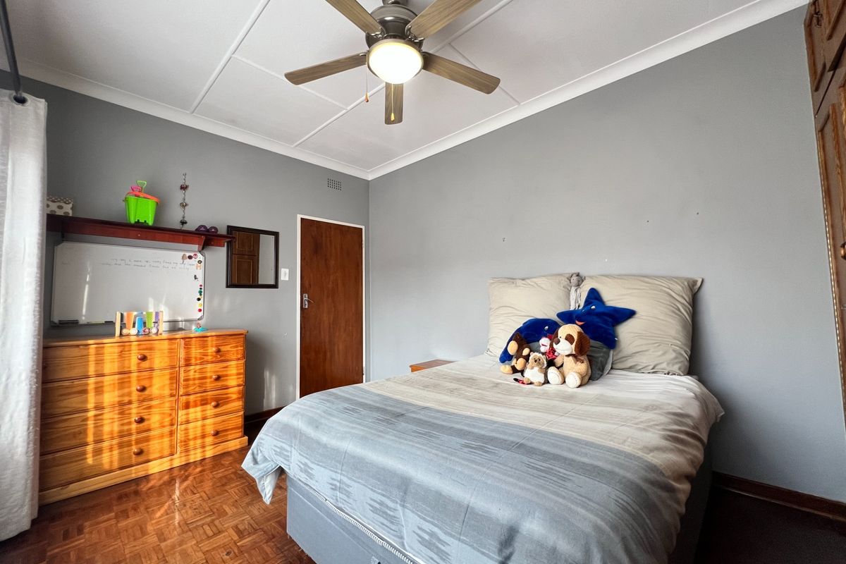 A bedroom featuring parquet flooring, a ceiling fan, and built-in cupboard storage, finished with neutral grey walls and coved ceiling detailing.