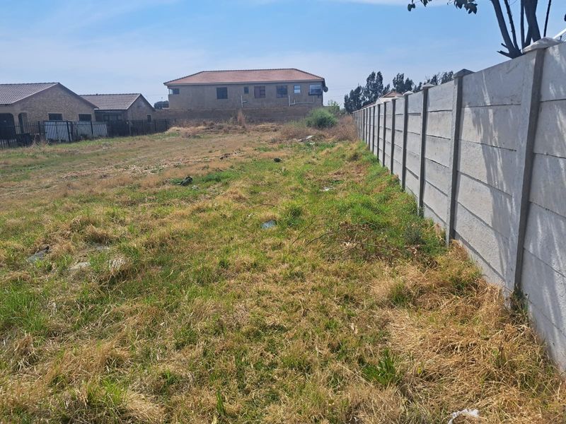 A vacant residential plot featuring a precast concrete boundary wall and natural grass coverage, suitable for future development.