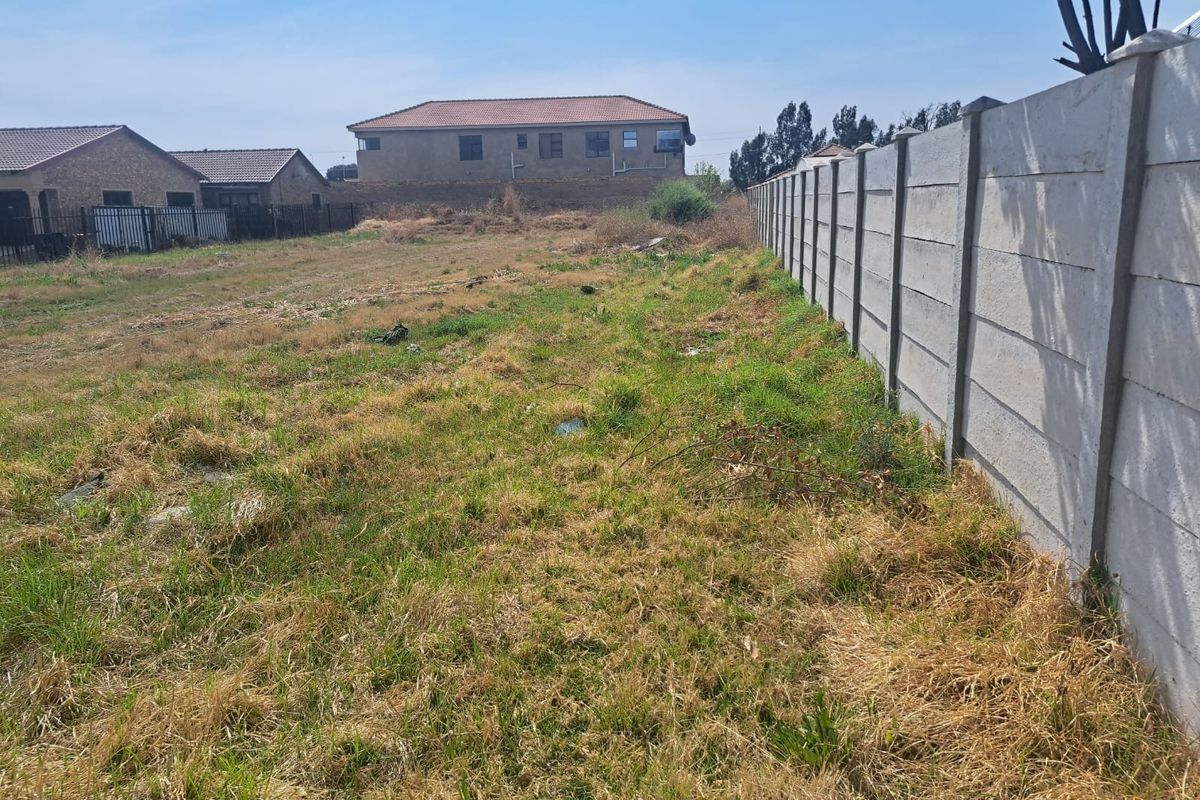 A vacant residential plot featuring a precast concrete boundary wall and natural grass coverage, suitable for future development.