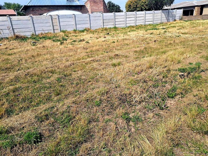 A view of a vacant residential plot featuring dry grass and a precast concrete boundary wall.