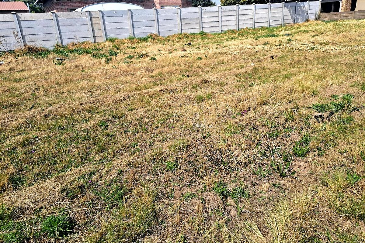 A view of a vacant residential plot featuring dry grass and a precast concrete boundary wall.