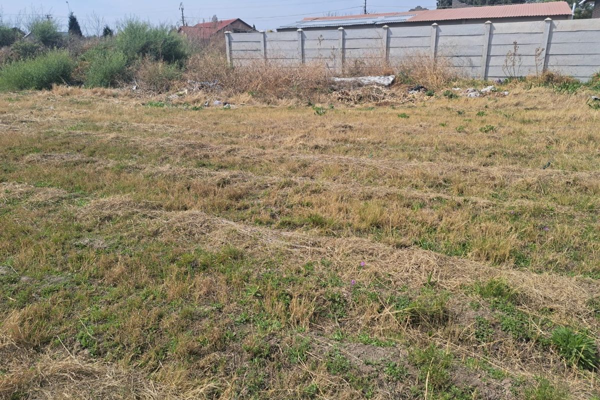 A vacant residential plot featuring dry grass and a precast concrete boundary wall at the rear.