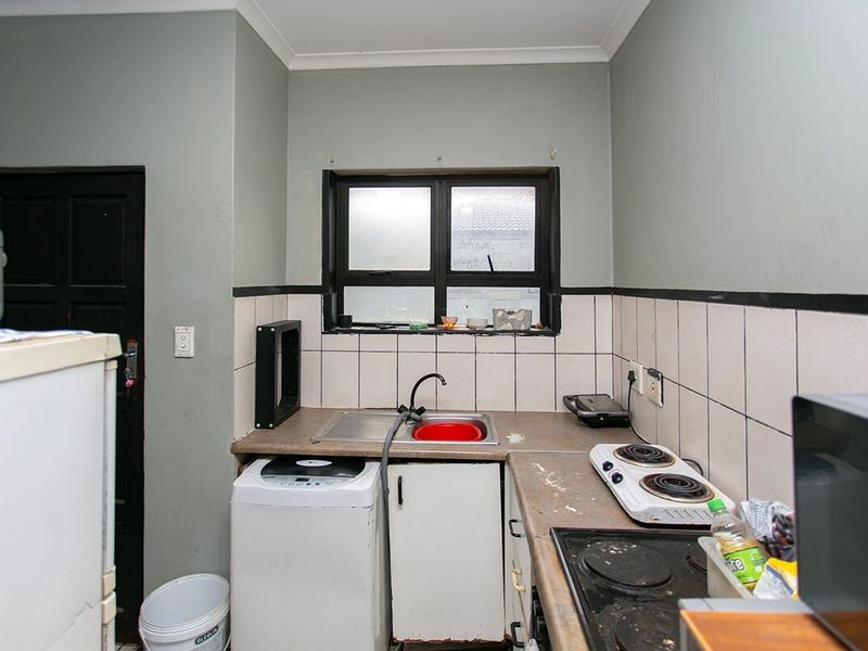 A compact kitchen featuring a stainless steel sink, tiled splashback, and built-in cabinetry with a laminate countertop and electric hob.