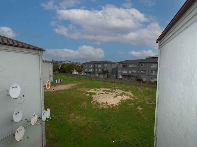 An elevated view looking out over a communal grassy area between apartment blocks, featuring multiple satellite dishes mounted on the exterior wall.