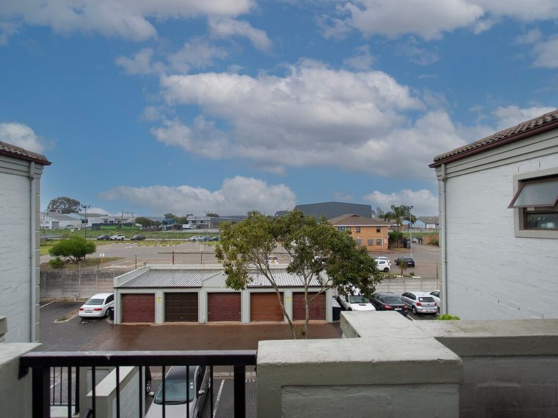 An elevated view from a balcony overlooking a parking area, garage units, and surrounding neighborhood landscape.