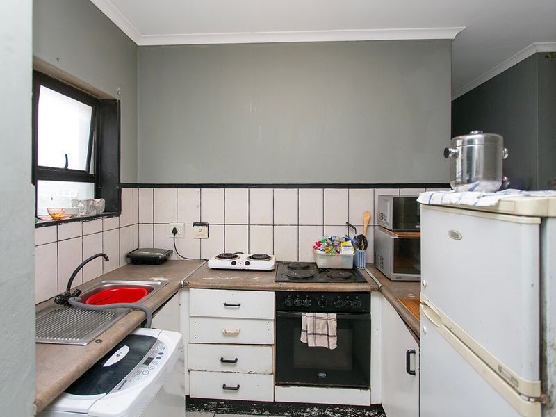 Compact kitchen featuring a built-in oven, electric hob, stainless steel sink, and tiled backsplash, offering a functional layout with potential for modernization.