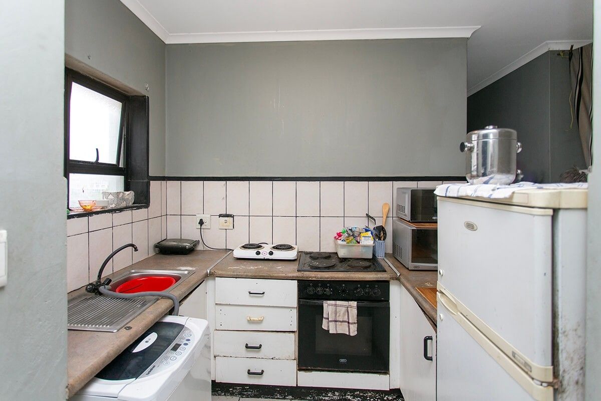 Compact kitchen featuring a built-in oven, electric hob, stainless steel sink, and tiled backsplash, offering a functional layout with potential for modernization.