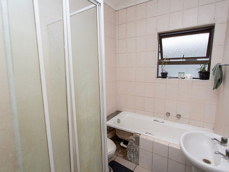 A dated bathroom featuring a shower enclosure, bathtub, and pedestal basin, currently requiring maintenance and cosmetic updates to the tiling and bathtub surround.