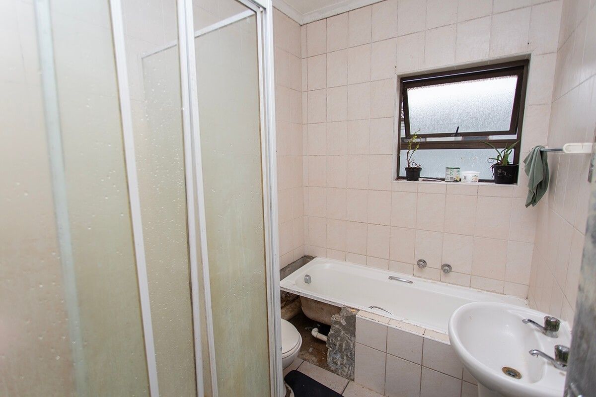 A dated bathroom featuring a shower enclosure, bathtub, and pedestal basin, currently requiring maintenance and cosmetic updates to the tiling and bathtub surround.