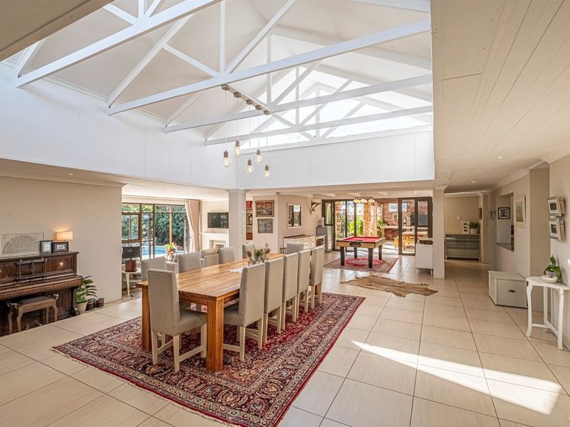 Spacious open-plan living and dining area featuring high vaulted ceilings with exposed white trusses, abundant natural light, and large sliding doors leading outdoors.