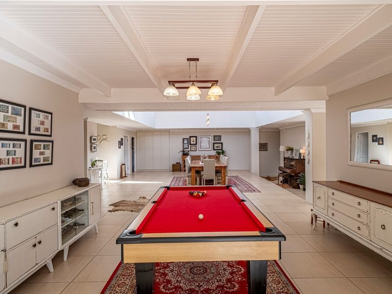 Spacious open-plan living area featuring a beamed ceiling, tiled flooring, and a large skylight, creating a bright and versatile entertainment space.