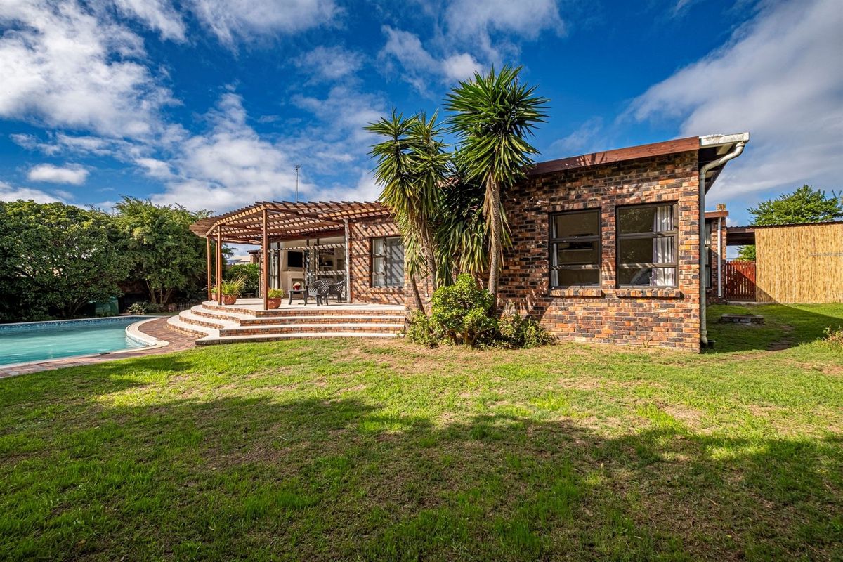 Rear view of the property featuring a brick facade, a covered timber pergola patio, and a swimming pool set within a landscaped garden.