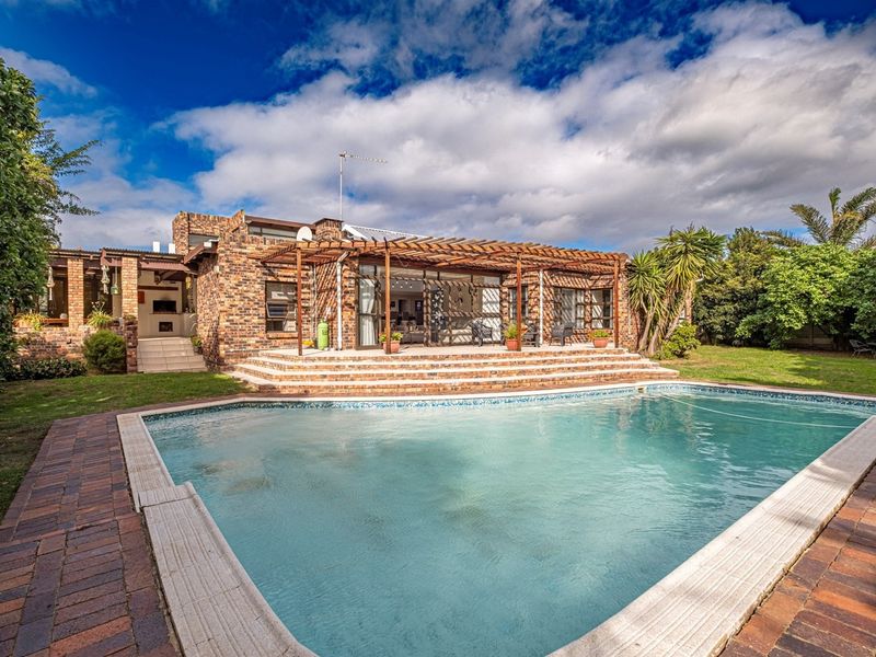 Rear exterior view featuring a swimming pool, paved patio area, timber pergola, and a face-brick facade with an integrated outdoor fireplace.