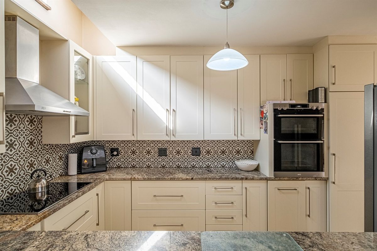 A well-maintained kitchen featuring shaker-style cabinetry, granite countertops, a decorative patterned backsplash, and integrated stainless steel appliances including a double oven and extractor fan.
