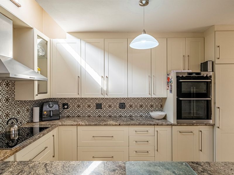 A well-maintained kitchen featuring shaker-style cabinetry, granite countertops, a decorative patterned backsplash, and integrated stainless steel appliances including a double oven and extractor fan.