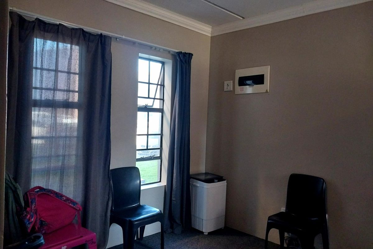 A living area featuring neutral wall tones, a casement window with curtains, and a wall-mounted electrical distribution board.