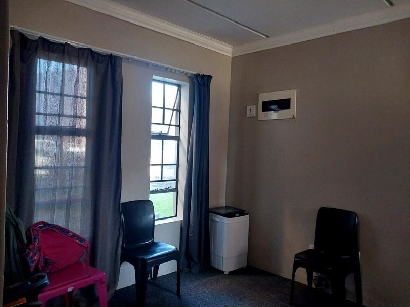 A living area featuring neutral wall tones, a casement window with curtains, and a wall-mounted electrical distribution board.