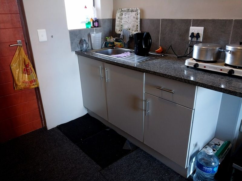 Compact kitchen area featuring modern grey cabinetry, granite countertops, a stainless steel sink, and a tiled backsplash with an integrated electric hob.