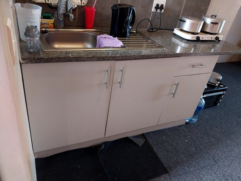 A compact kitchen area featuring a stainless steel sink, granite countertop, and neutral-toned built-in cabinetry with a tiled backsplash.