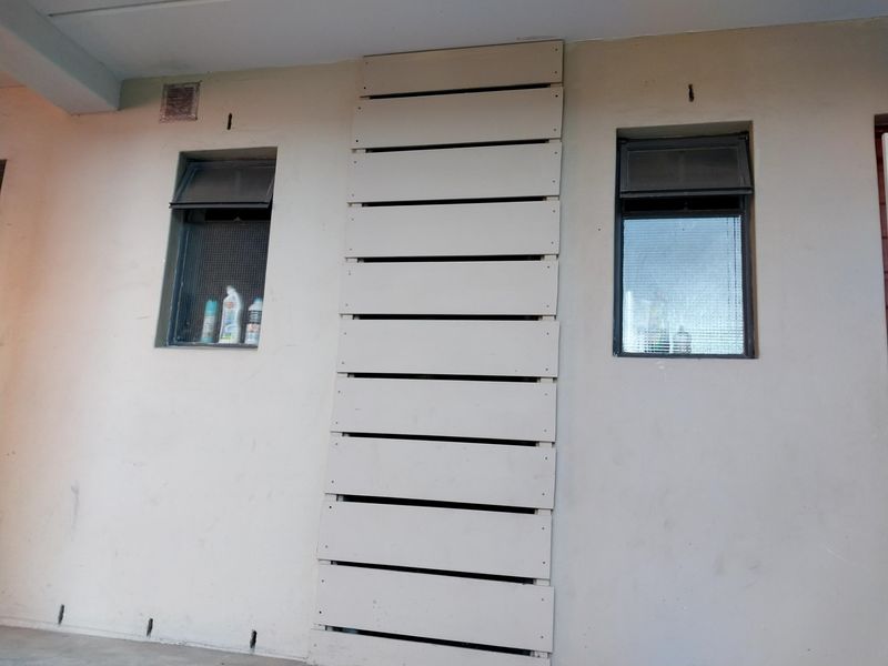 Exterior wall section featuring two top-hung windows with security screens and a central decorative timber slat panel.