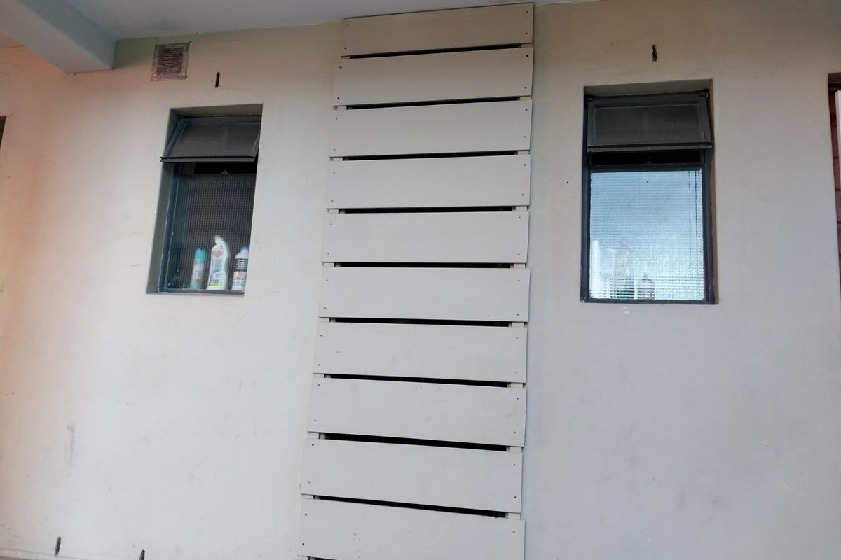 Exterior wall section featuring two top-hung windows with security screens and a central decorative timber slat panel.