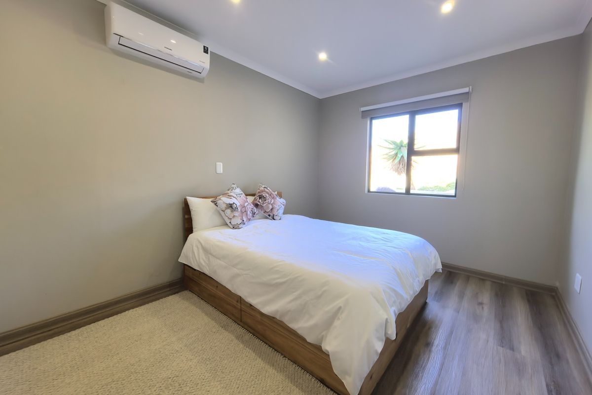 A well-maintained bedroom featuring modern laminate flooring, recessed downlighting, and a wall-mounted split-system air conditioning unit.