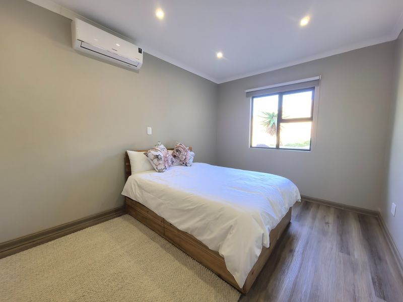 A well-maintained bedroom featuring modern laminate flooring, recessed downlighting, and a wall-mounted split-system air conditioning unit.