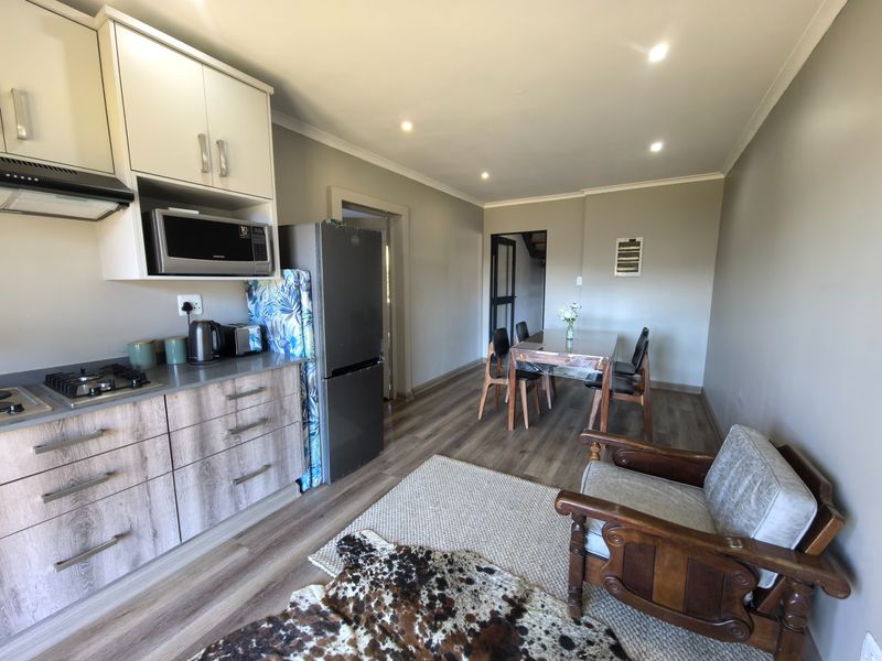 Modern open-plan living area featuring a compact kitchen with built-in cabinetry, gas hob, and integrated extractor, flowing into a dining space with laminate flooring.