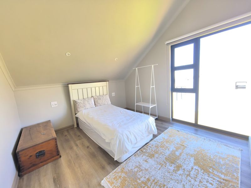 A bright bedroom featuring laminate flooring, a sloped ceiling with recessed lighting, and a large aluminium sliding door providing natural light.