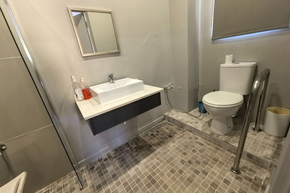 A functional bathroom featuring a wall-mounted vanity with a vessel sink, a toilet, and a shower enclosure with mosaic floor tiling.