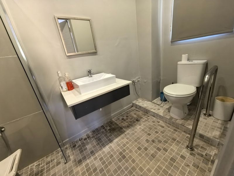 A functional bathroom featuring a wall-mounted vanity with a vessel sink, a toilet, and a shower enclosure with mosaic floor tiling.