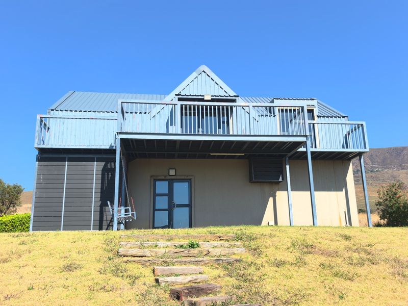 Rear view of a two-story house featuring a metal roof, a raised balcony with railings, and timber sleeper steps leading to the entrance.