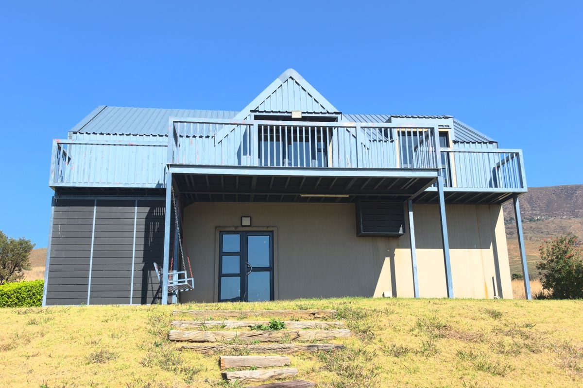 Rear view of a two-story house featuring a metal roof, a raised balcony with railings, and timber sleeper steps leading to the entrance.
