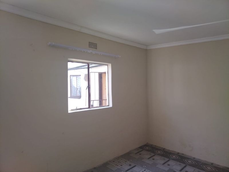 An empty bedroom featuring tiled flooring, a steel window with security bars, and a neutral wall finish, ready for personalization.