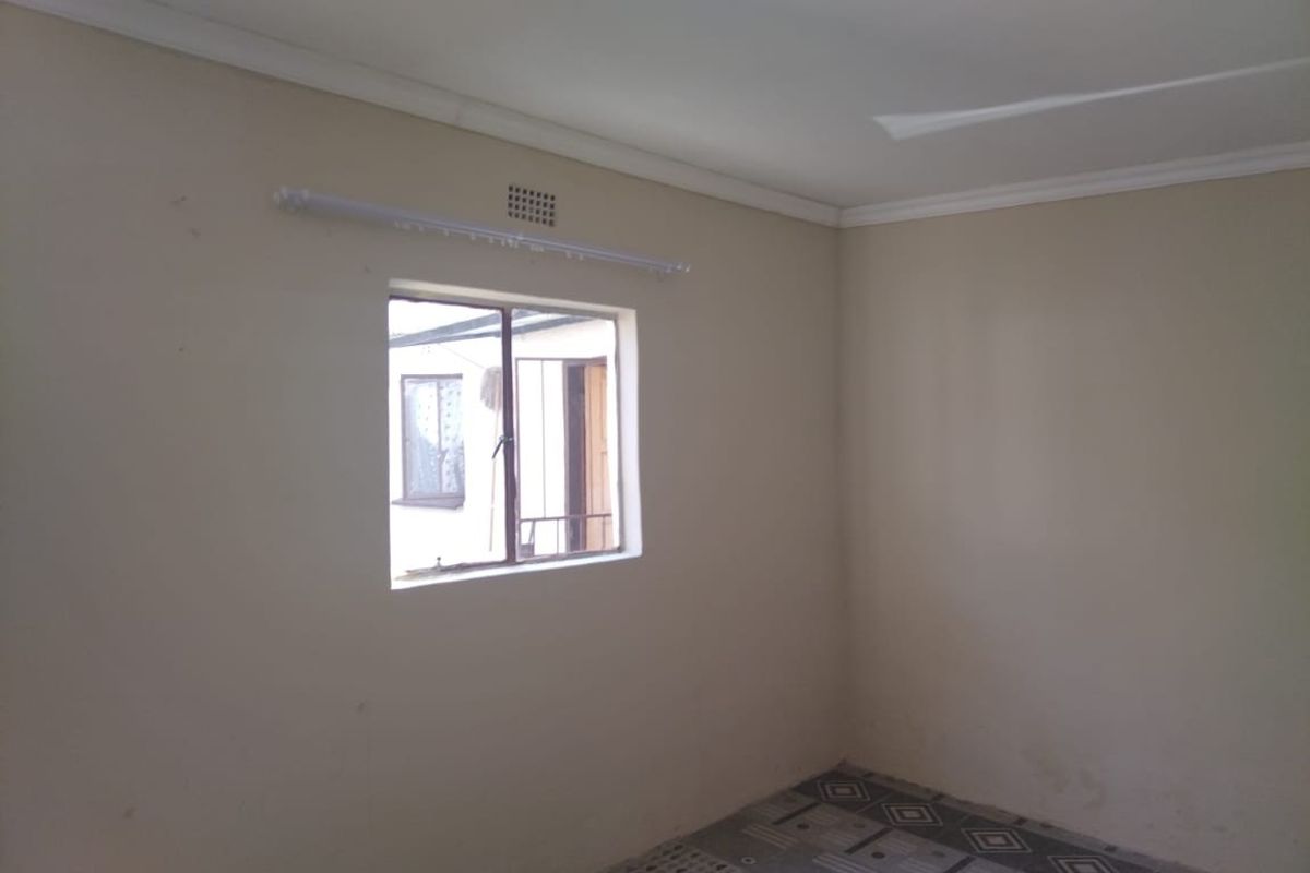 An empty bedroom featuring tiled flooring, a steel window with security bars, and a neutral wall finish, ready for personalization.