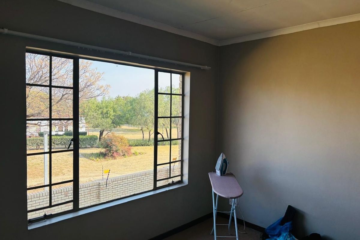 A vacant bedroom featuring a large steel-framed window with views of the garden, carpeted flooring, and neutral wall tones.