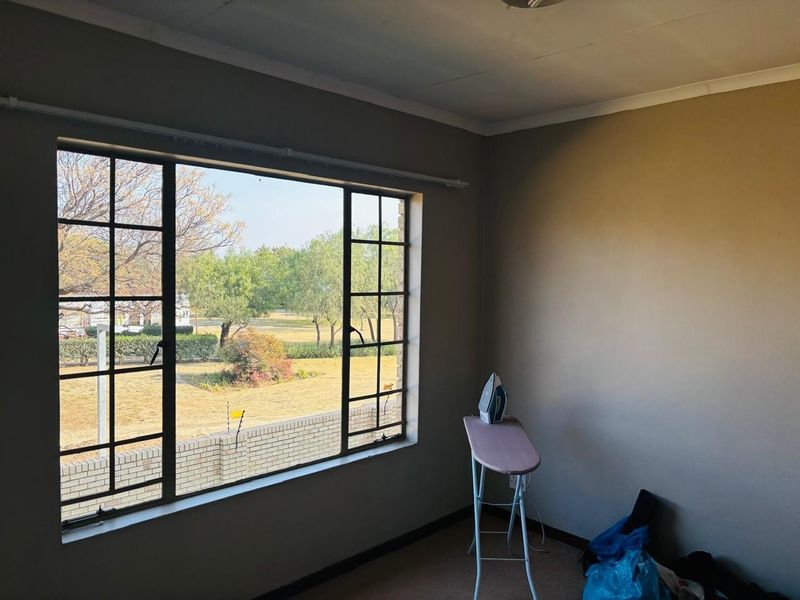 A vacant bedroom featuring a large steel-framed window with views of the garden, carpeted flooring, and neutral wall tones.