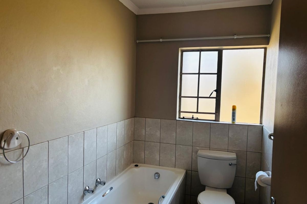 A functional bathroom featuring a built-in bathtub, toilet, and tiled splashback, offering a neutral canvas for potential cosmetic updates.
