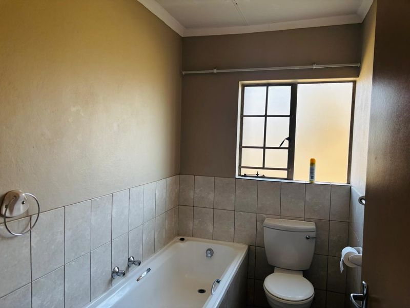 A functional bathroom featuring a built-in bathtub, toilet, and tiled splashback, offering a neutral canvas for potential cosmetic updates.