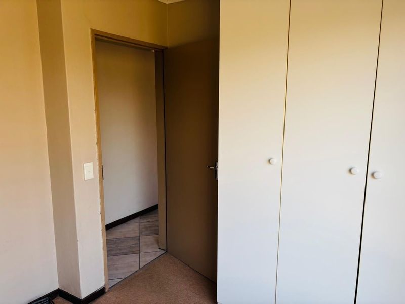 A bedroom featuring built-in cupboards, carpeted flooring, and an internal door leading to a tiled hallway.