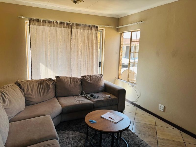 A living room featuring tiled flooring, a sliding glass door, and security bars on the window, requiring cosmetic updates to the walls and finishes.