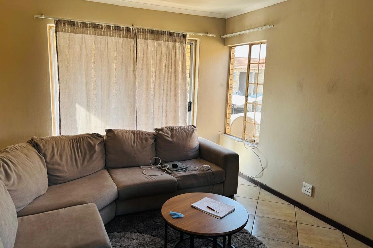 A living room featuring tiled flooring, a sliding glass door, and security bars on the window, requiring cosmetic updates to the walls and finishes.