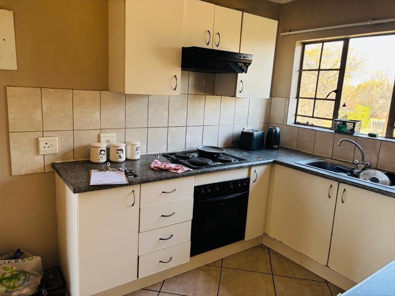 A functional kitchen featuring built-in cabinetry, a tiled backsplash, an electric hob with extractor fan, and a stainless steel sink.