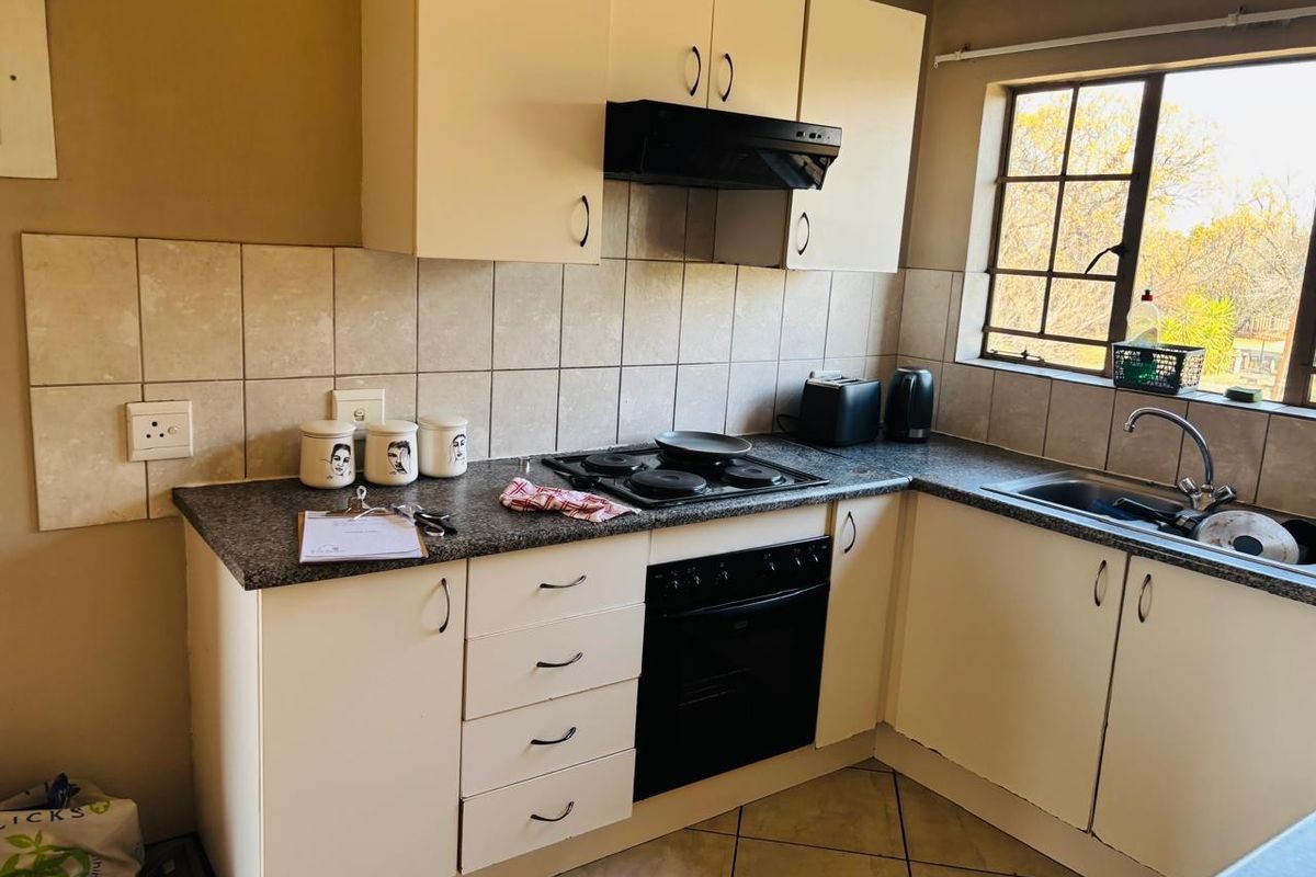 A functional kitchen featuring built-in cabinetry, a tiled backsplash, an electric hob with extractor fan, and a stainless steel sink.