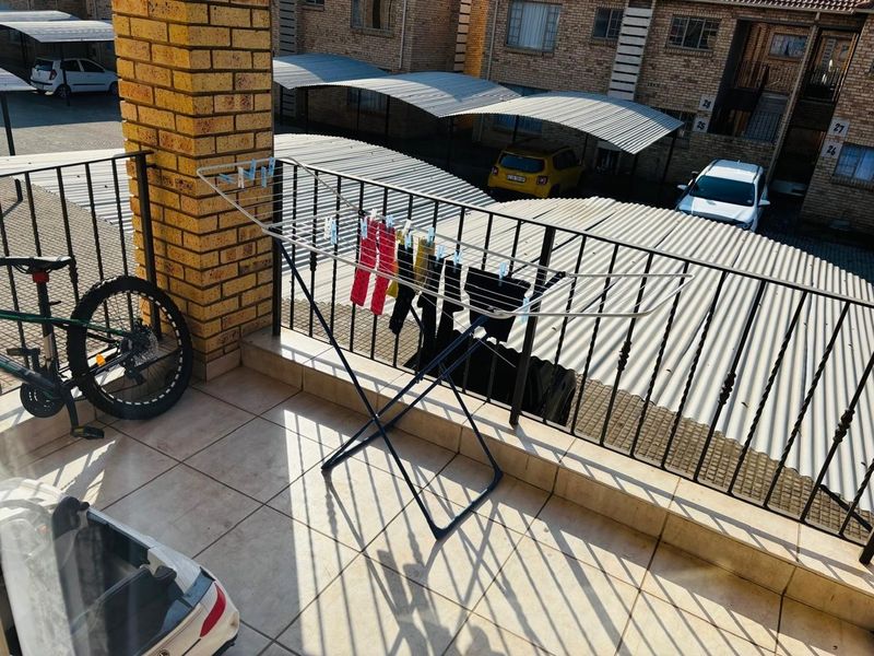 A functional balcony area featuring tiled flooring and a metal balustrade, overlooking the apartment complex parking area.