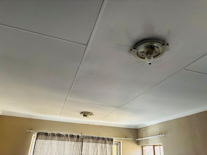 A view of a living room ceiling featuring basic flush mount lighting, coving, and curtain rails, showing signs of wear and dated finishes.
